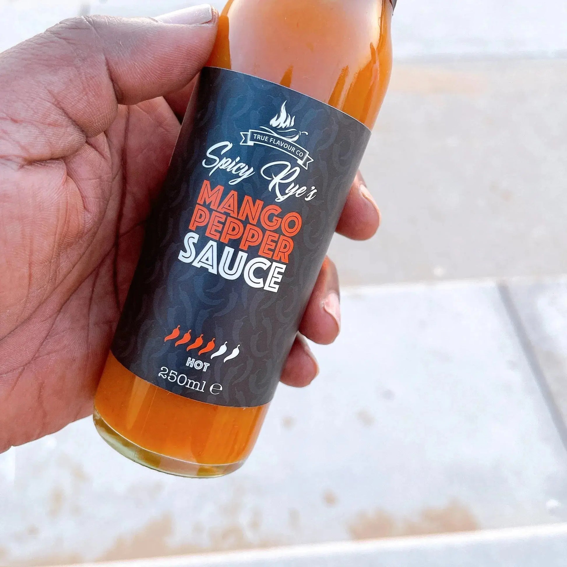 Spicy Ryes Mango Pepper Hot Sauce bottle with bright label and fresh mango and peppers around it.