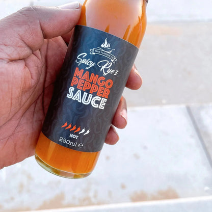 Spicy Ryes Mango Pepper Hot Sauce bottle with bright label and fresh mango and peppers around it.