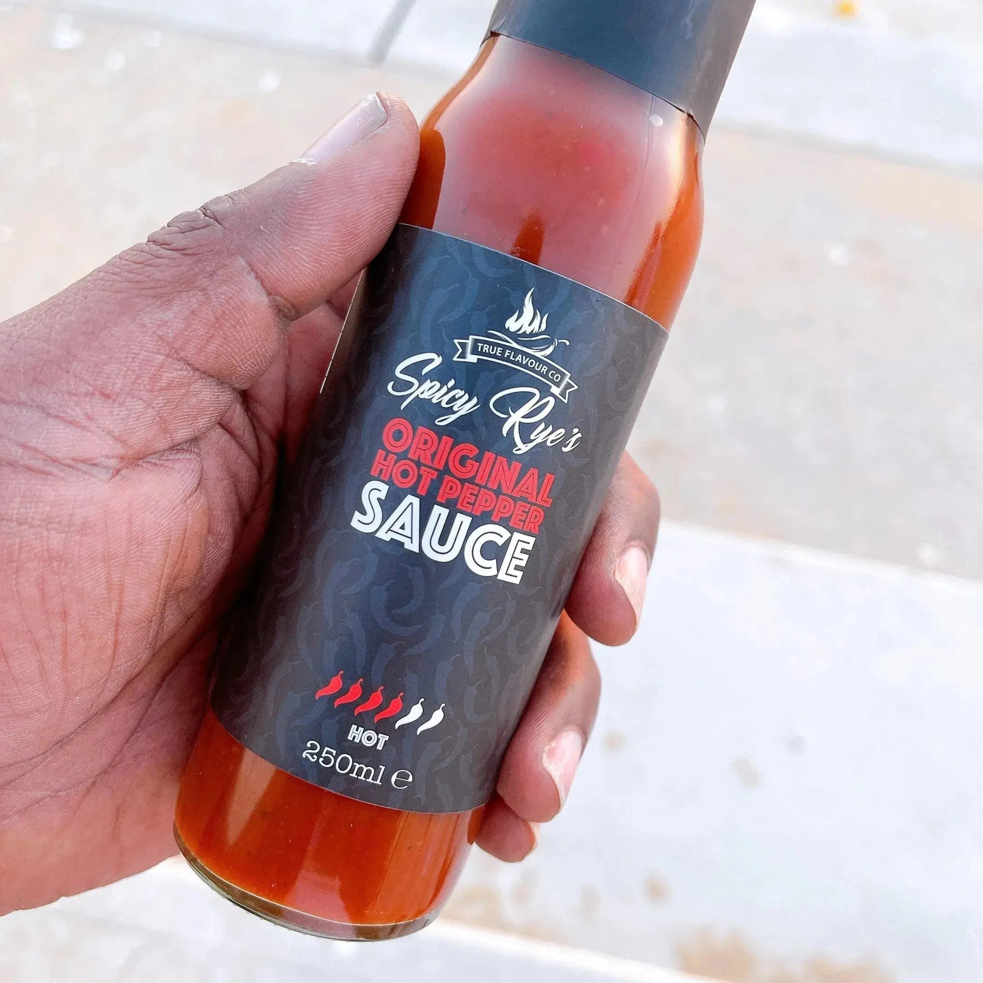 Spicy Ryes Original Hot Pepper Sauce bottle with bright red hot sauce visible in a glass bottle on a wooden surface.