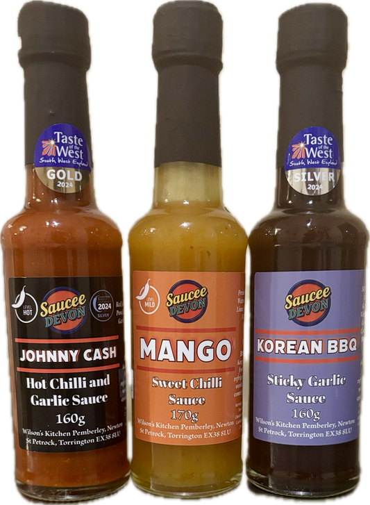 Wilson’s Kitchen Favourite Selection of artisan chilli sauces displayed in glass bottles on a wooden table.