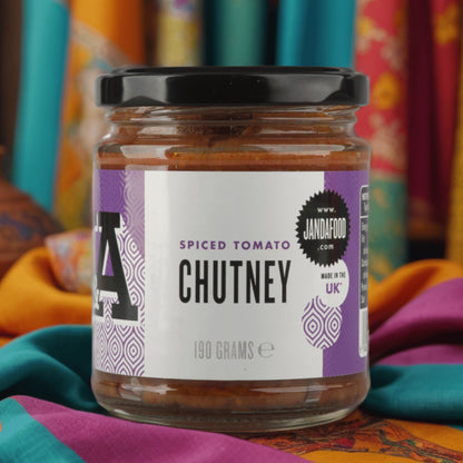 Janda Food Spiced Tomato Chutney in a glass jar with a purple label, set against a vibrant patterned fabric backdrop.