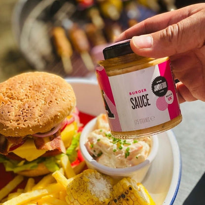 Janda Food vegan burger sauce jar held over a plate with a cheeseburger, fries, and corn at a barbecue