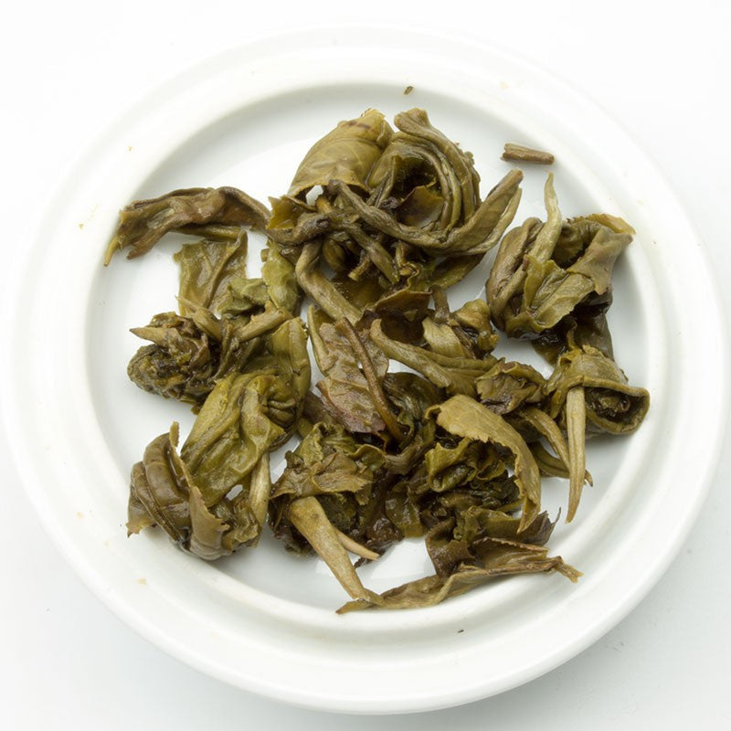 Brewed Jasmine Dragon Pearl Green Tea leaves by PekoeTea Edinburgh in a clear glass cup, showcasing fresh green tea and jasmine pearls.