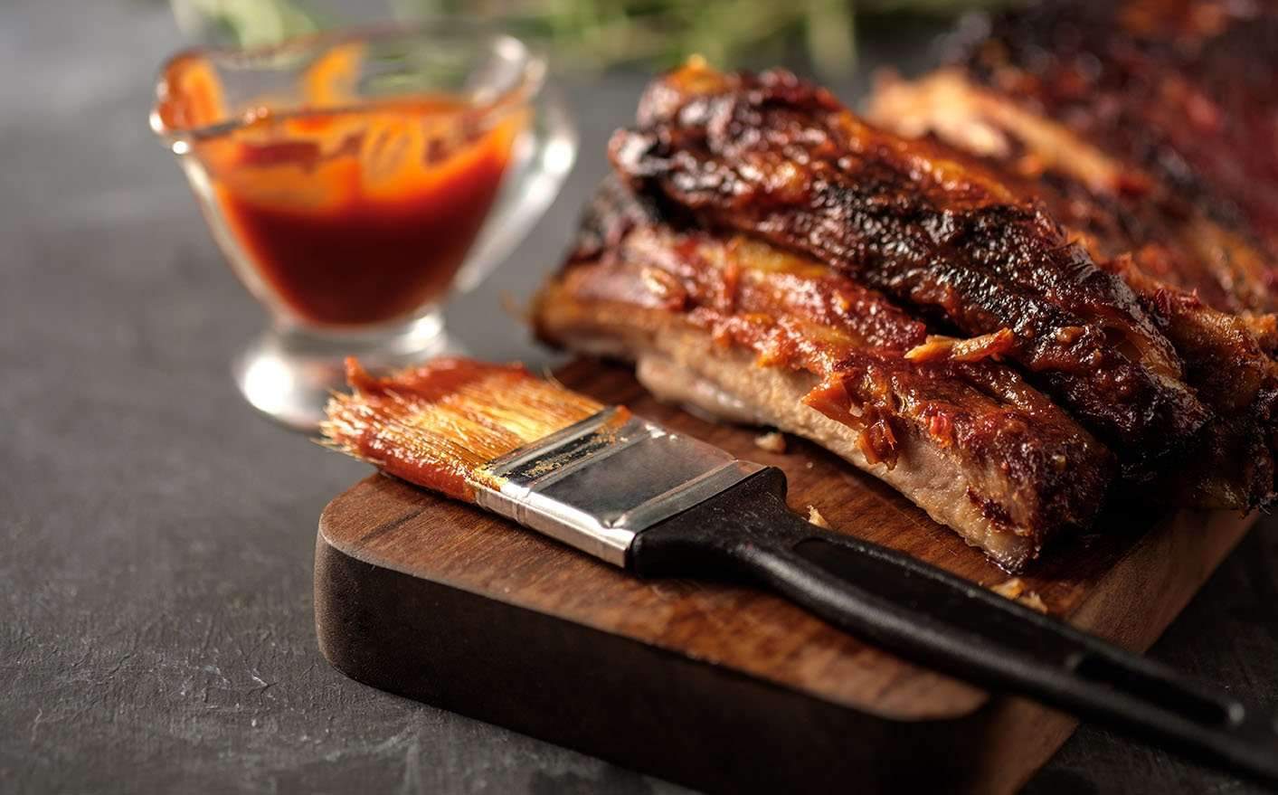 Bottle of FireFly Barbecue Louisiana BBQ Sauce with rib and wing dishes on a wooden table, showcasing rich, smoky flavor.