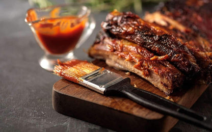 Bottle of FireFly Barbecue Louisiana BBQ Sauce with rib and wing dishes on a wooden table, showcasing rich, smoky flavor.