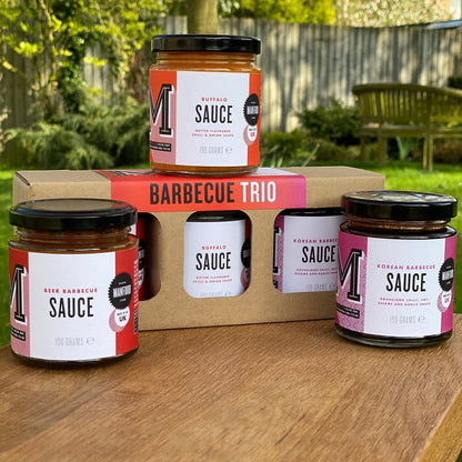 Manfood BBQ Trio gift box featuring Beer, Korean, and Buffalo barbecue sauces in glass jars on a wooden table.