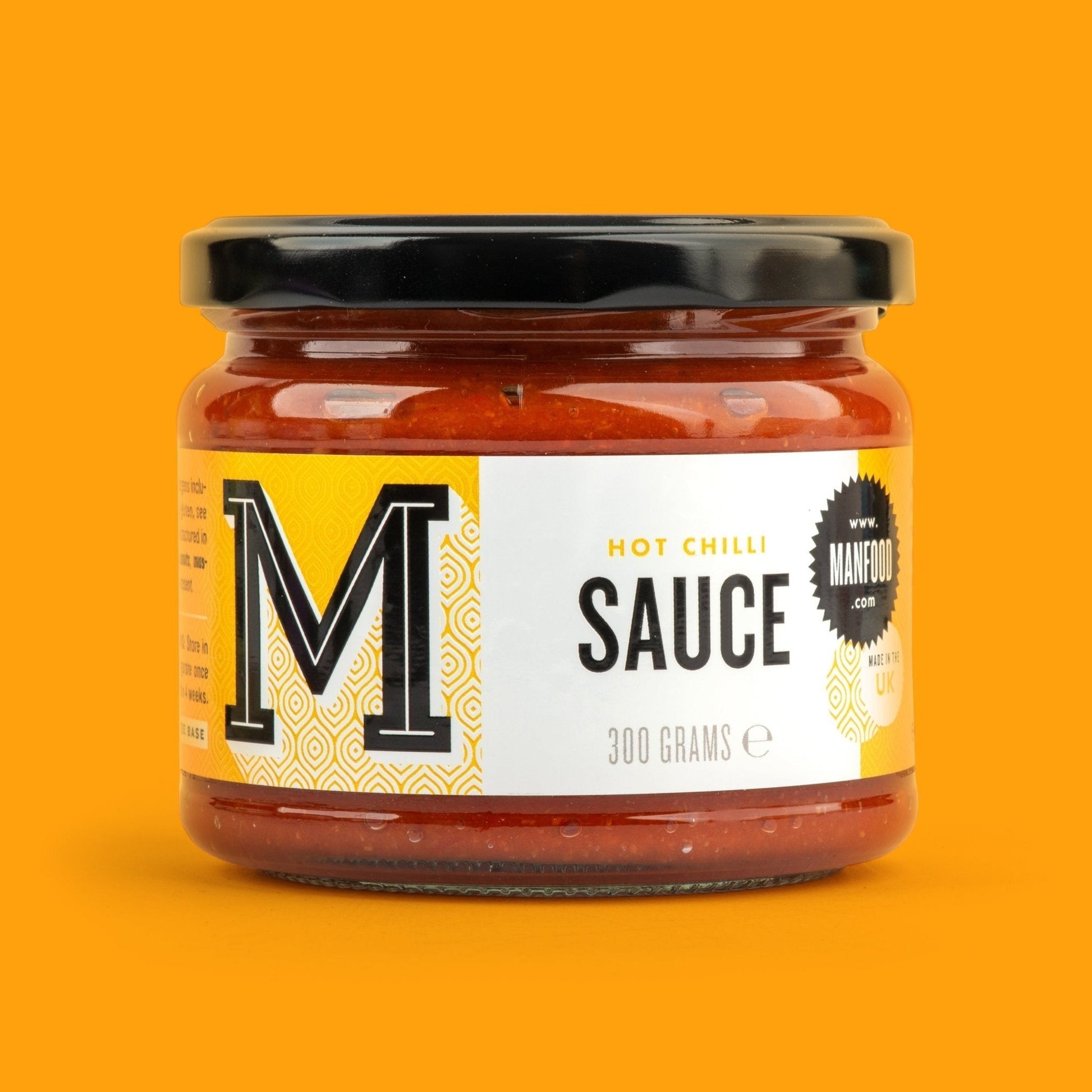 Manfood hot chilli sauce in a 300g glass jar with a black lid against a vibrant orange background.