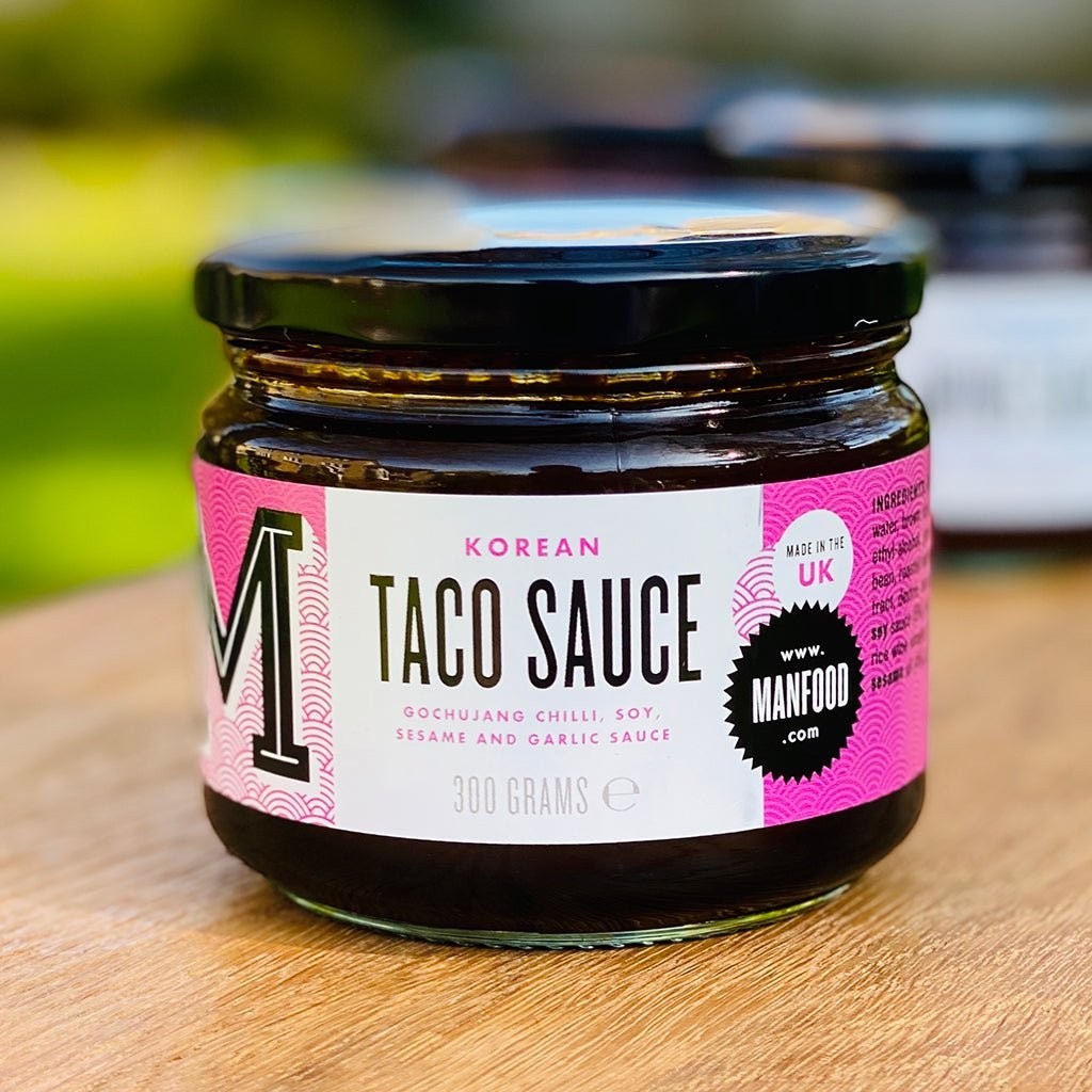 Manfood Korean Taco Sauce in a glass jar with a vibrant pink label featuring gochujang, soy, and sesame.