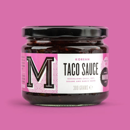 Manfood Korean Taco Sauce in a glass jar with a pink label featuring gochujang, soy, sesame, and garlic.