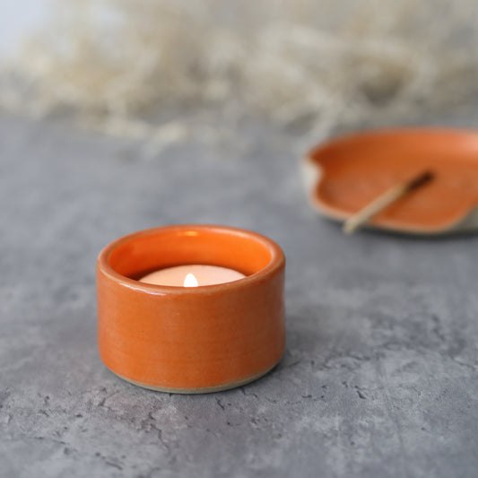 Orange square tea light holder by Katie L Thompson Designs with a lit tealight, showcasing a warm glowing ambiance.