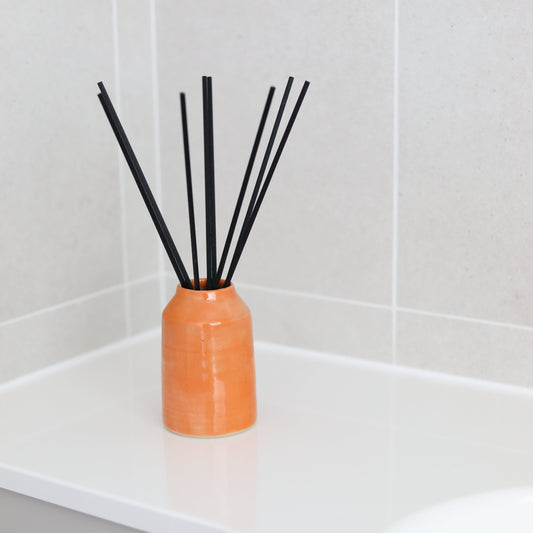 Mandarin orange reed diffuser by Katie L Thompson Designs with a sleek glass bottle and natural reed sticks for home fragrance.