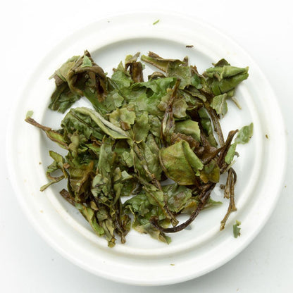 Brewed Pai Mu Dan white tea in a glass cup, showcasing delicate white tea leaves and a light, golden infusion in a PekoeTea Edinburgh mug