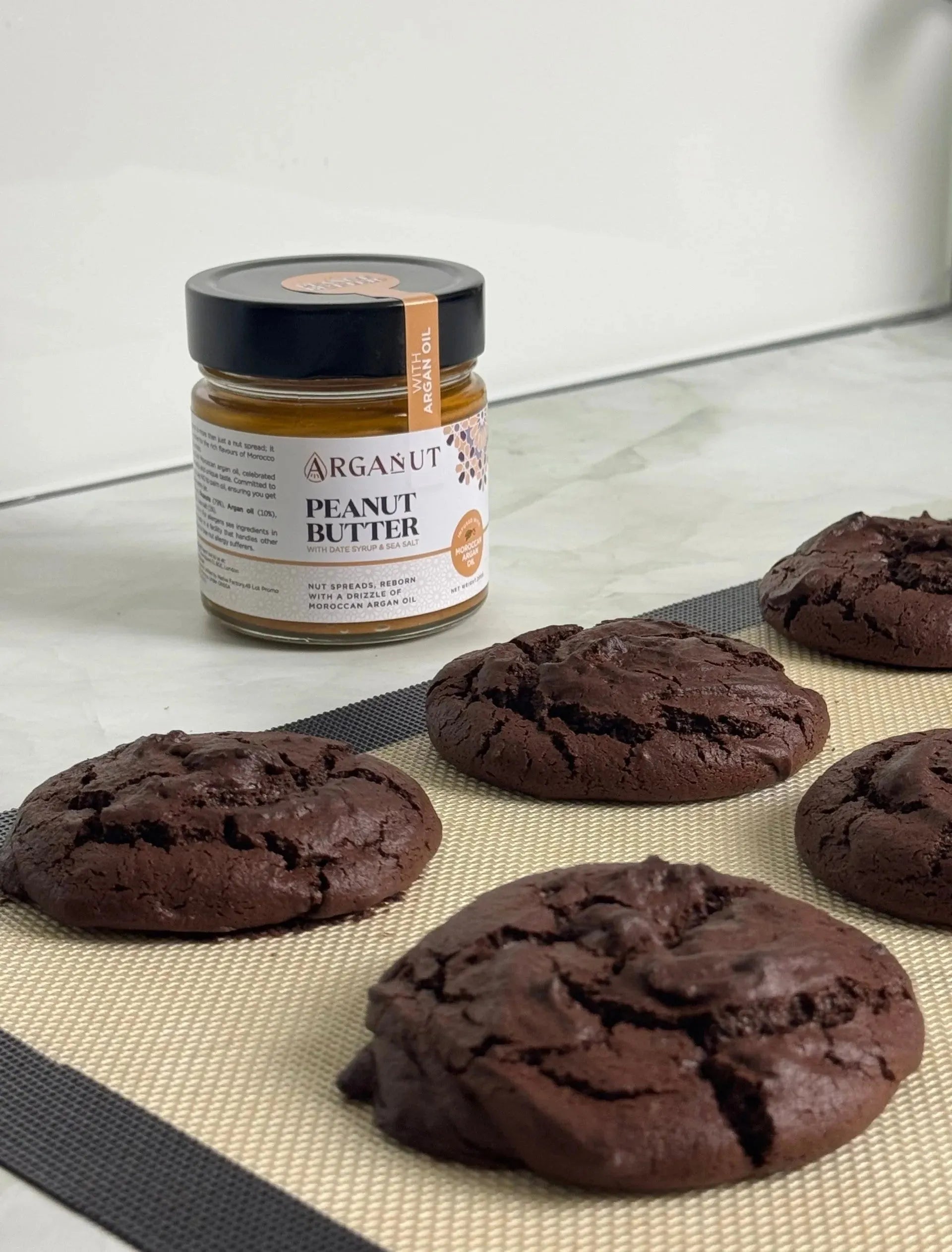 Smooth ArgaNut nut butter with peanut, argan oil, and date syrup in a 200g jar, shown with a spoon and spread on bread.
