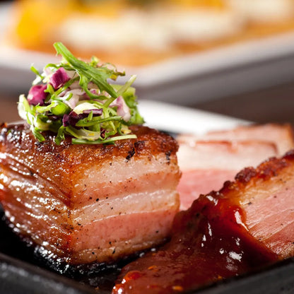 Cooked bone-in pork belly squares from Primrose Herd, showcasing crispy, golden-brown pork belly with visible layers of meat and fat.