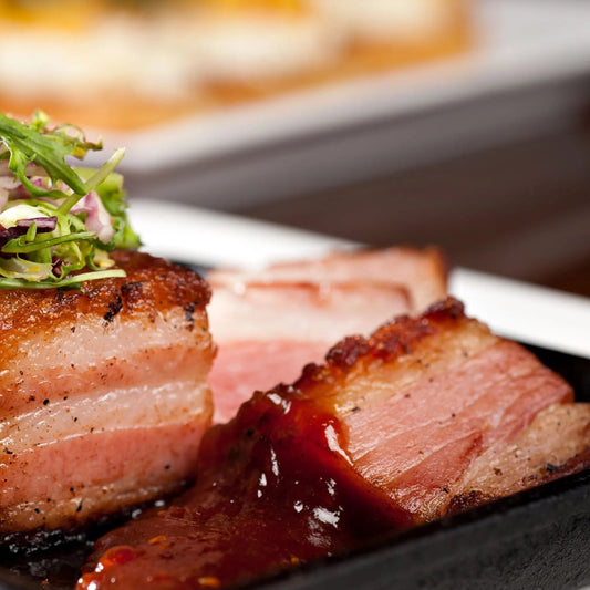 Cooked bone-in pork belly from Primrose Herd, showcasing crispy, golden-brown skin and tender meat on the bone.