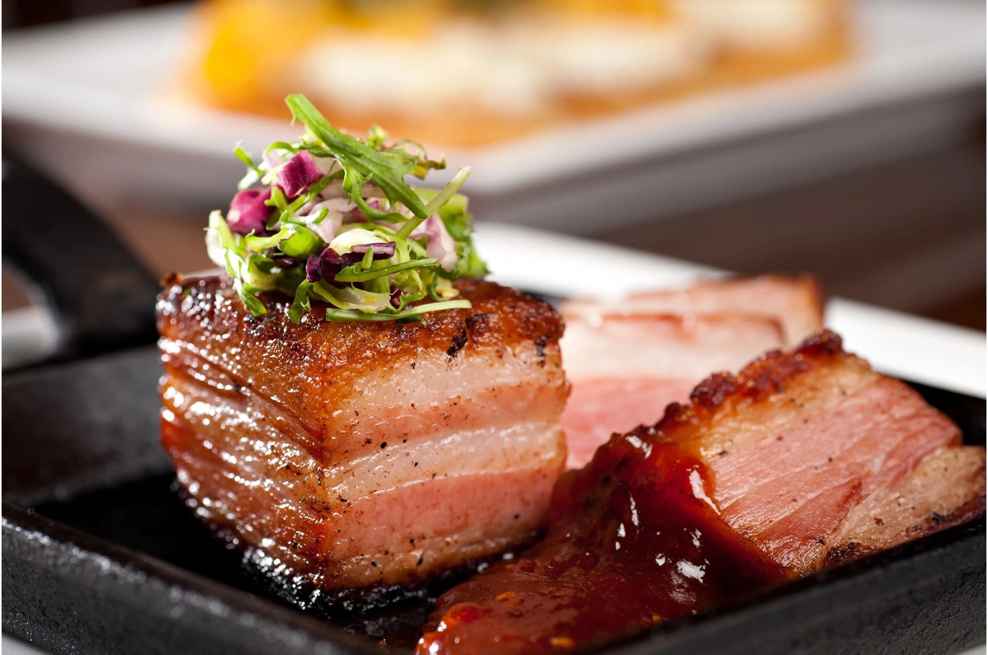 Cooked bone-in pork belly from Primrose Herd, showcasing crispy, golden-brown pork belly on the bone with visible crackling.