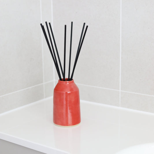 Cherry red reed diffuser by Katie L Thompson Designs in a stylish container, with natural reed sticks for home fragrance.