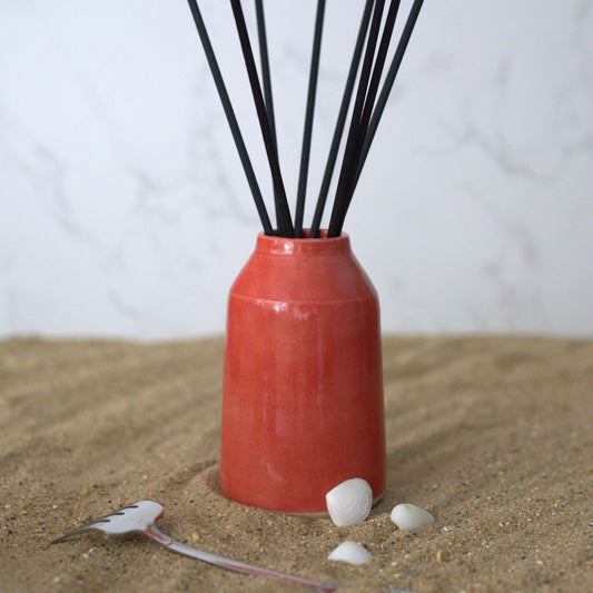 Cherry red classic reed diffuser by Katie L Thompson Designs with a square glass bottle and natural reed sticks.