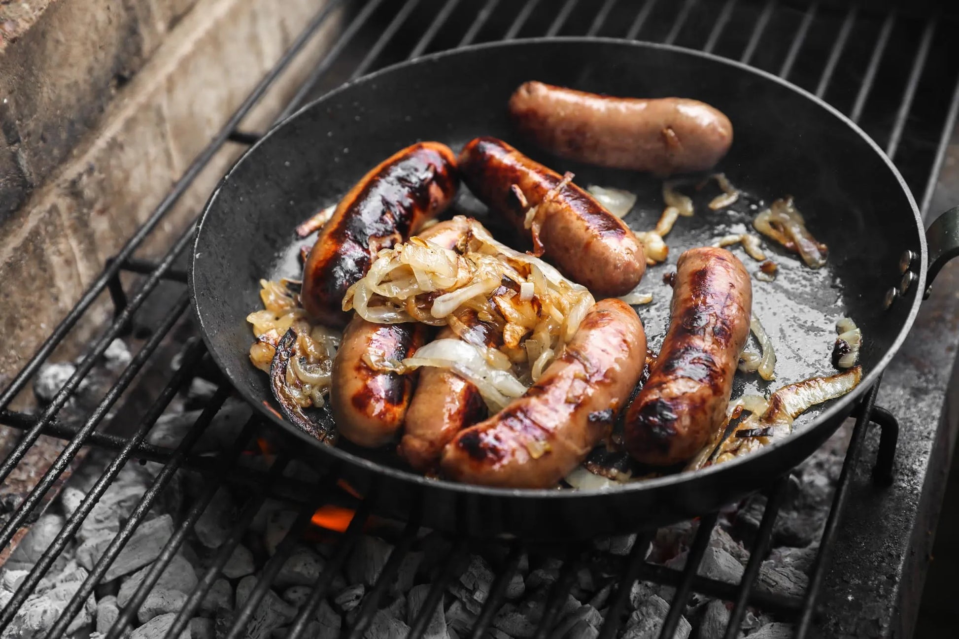 Primrose Herd cranberry and rosemary chipolata sausages cooking in a pan, showcasing their flavorful ingredients and golden-brown exterior.
