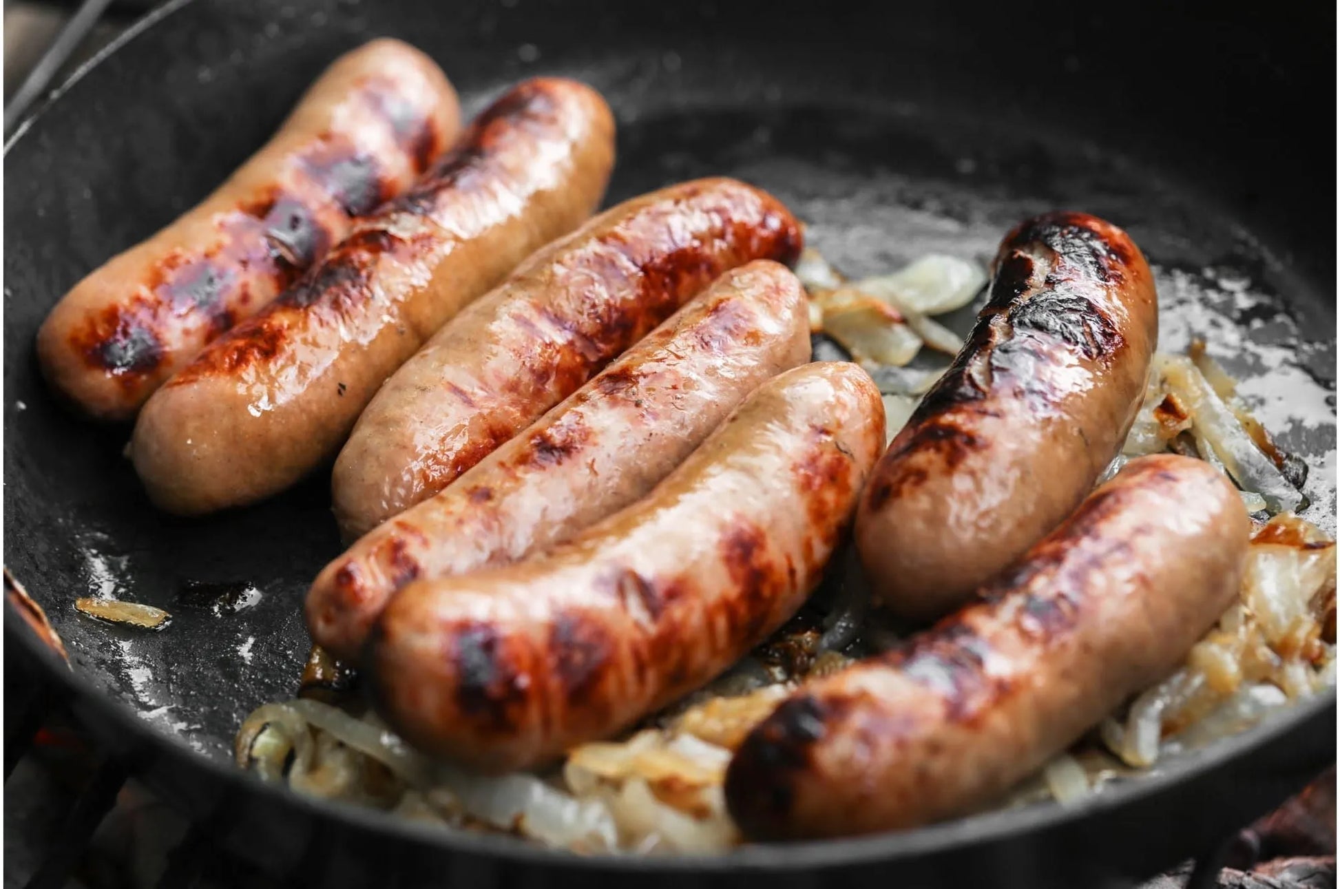 Primrose Herd pork sausages cooking in a pan, sizzling and browned, ready to serve as a delicious breakfast or meal.
