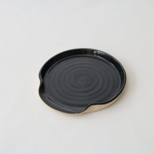 Jet black ceramic spoon rest by Katie L Thompson Designs, with a smooth, curved shape perfect for holding cooking utensils.