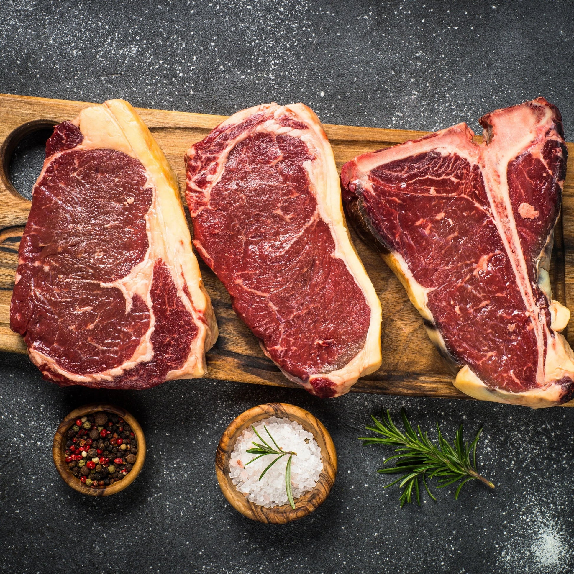 Three grass-fed beef steaks from Primrose Herd, fresh and juicy, displayed on a wooden cutting board.