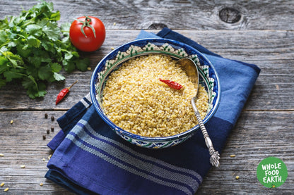 Organic bulgur wheat from Whole Food Earth, displayed in a clear bowl with loose grains on a wooden surface.