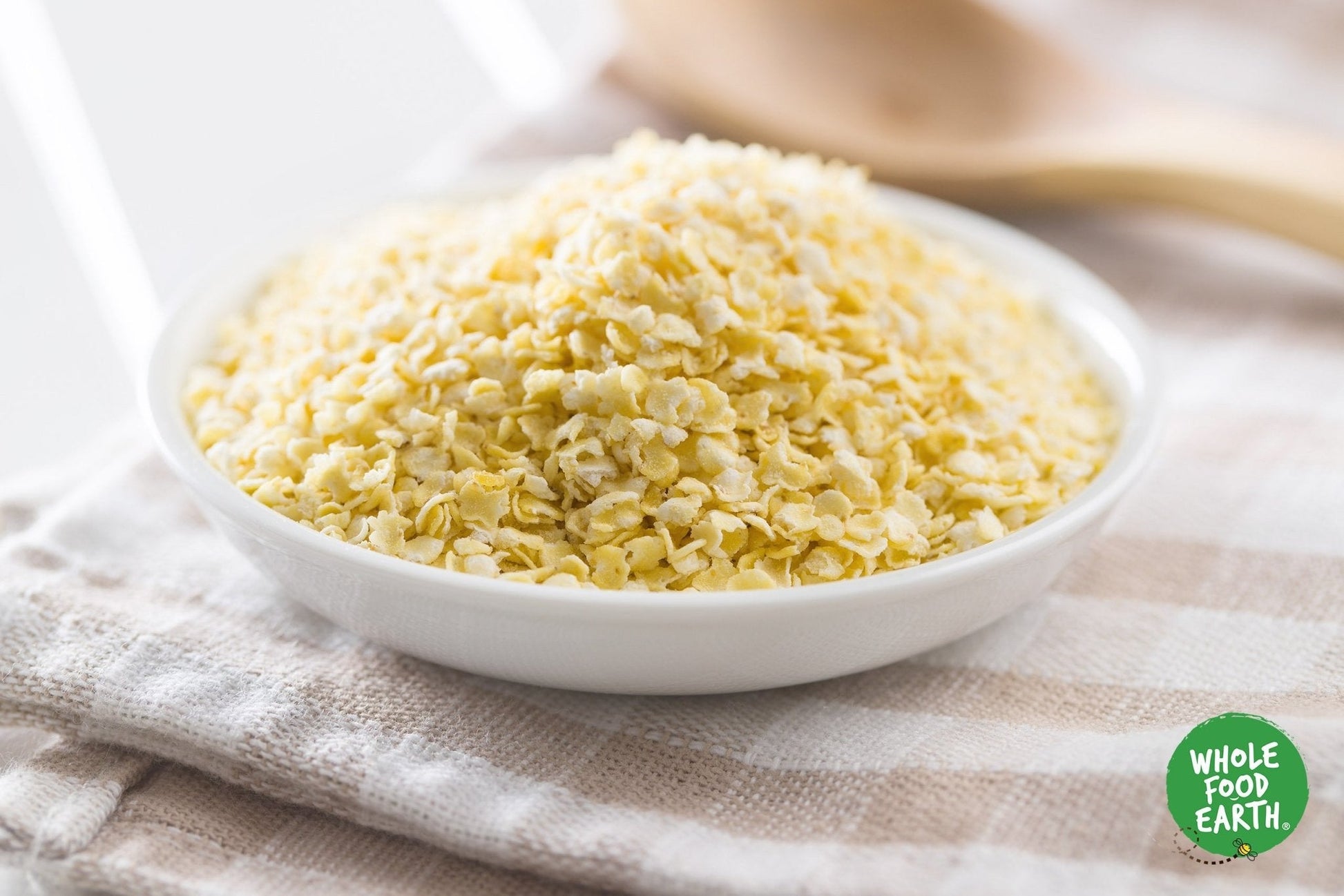 Organic millet flakes cereal by Whole Food Earth, close-up of golden, toasted millet flakes in a bowl on a white background.