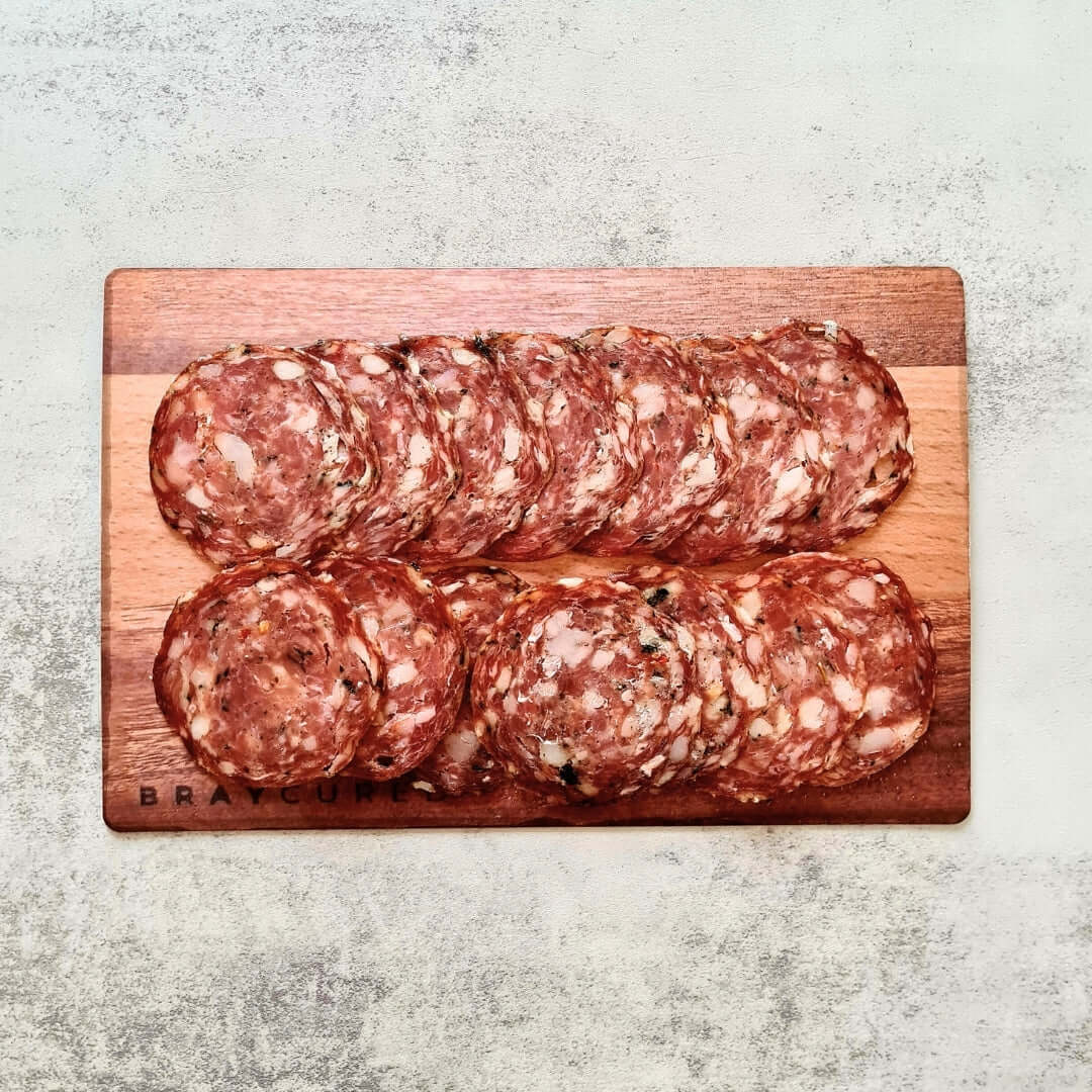 Sliced Bray Cured Wild Garlic Salami on a charcuterie board with cheese and crackers, showcasing its marbled texture and wild garlic flavor.